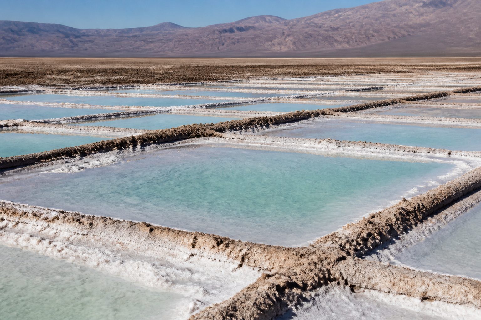 Pale evaporation ponds and white salt crust in morning sun.