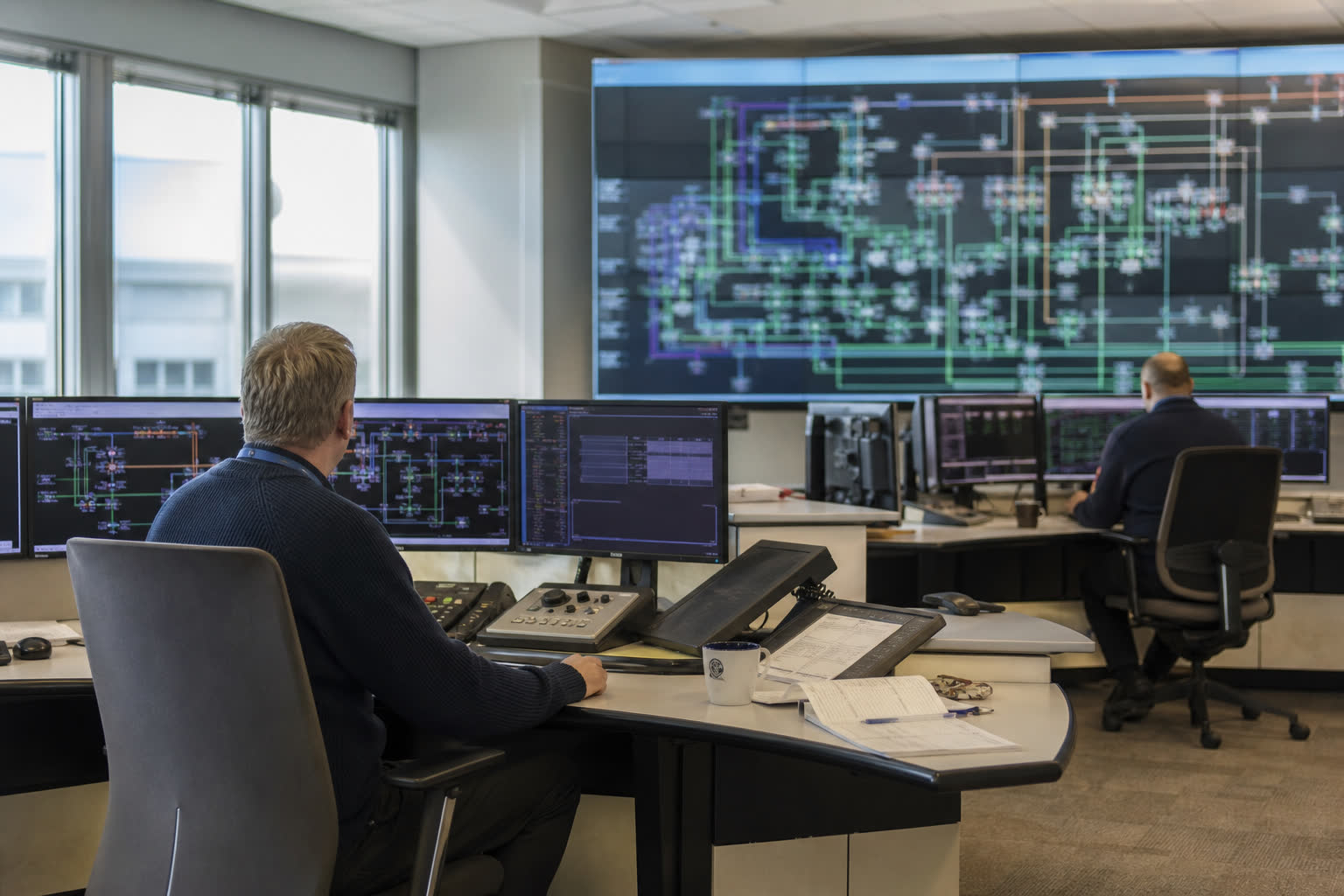 Two operators at screens, a wall map of the system behind them.