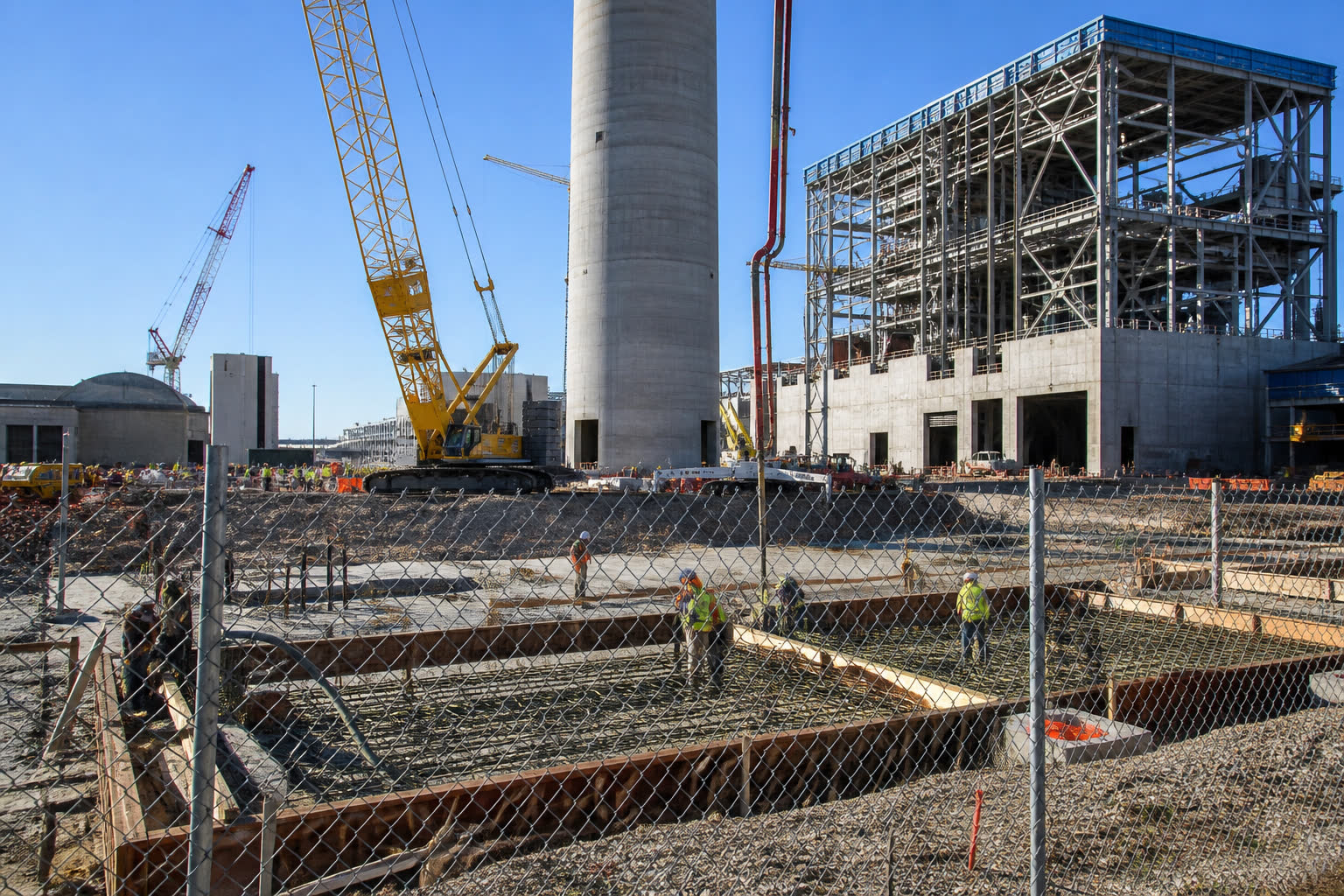 A plant going up behind a fence: crane, rebar, a concrete tower.