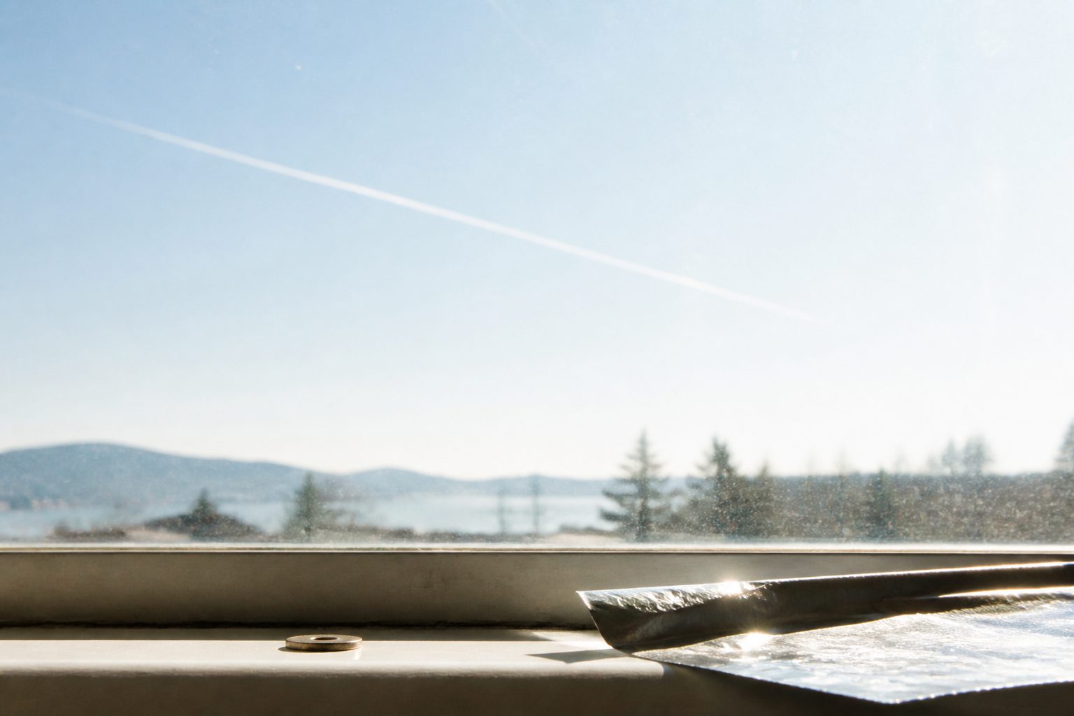 A window over water and hills, one contrail.