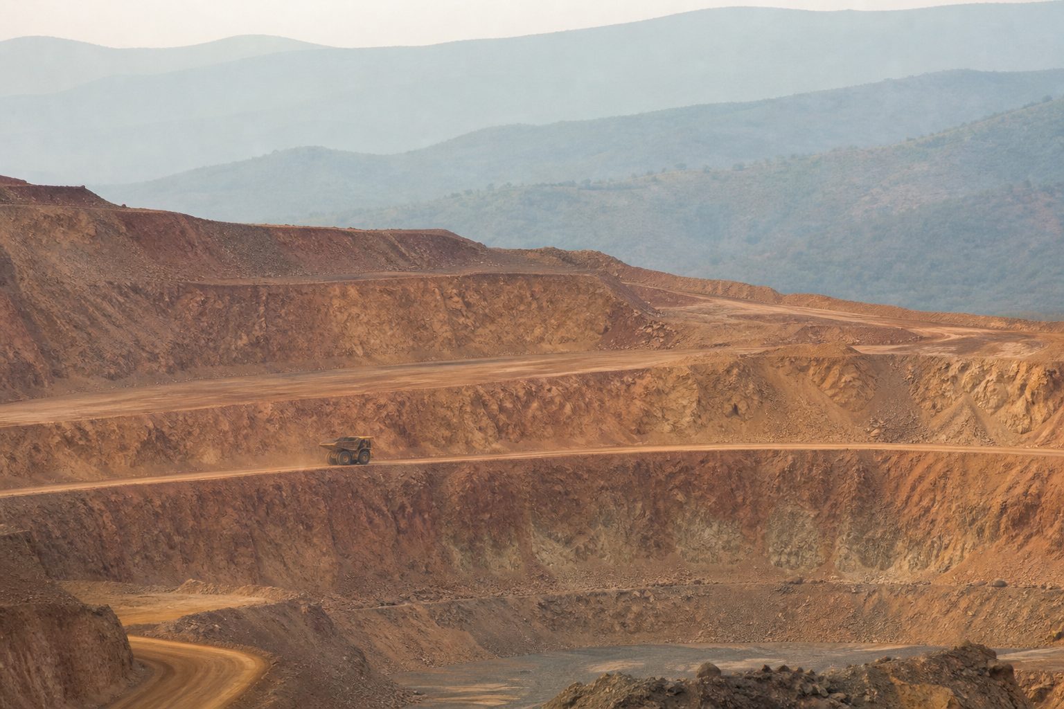 Orange mine terraces and one small haul truck in morning haze.