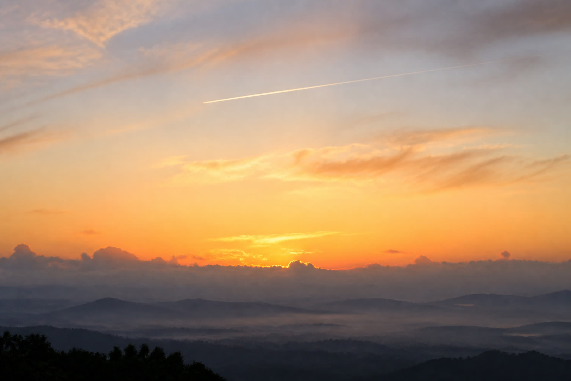 Hills in mist under a low sun, one contrail.
